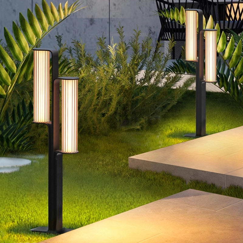 Two outdoor low lamps illuminate the stone path at night, standing on the lawn beside it.