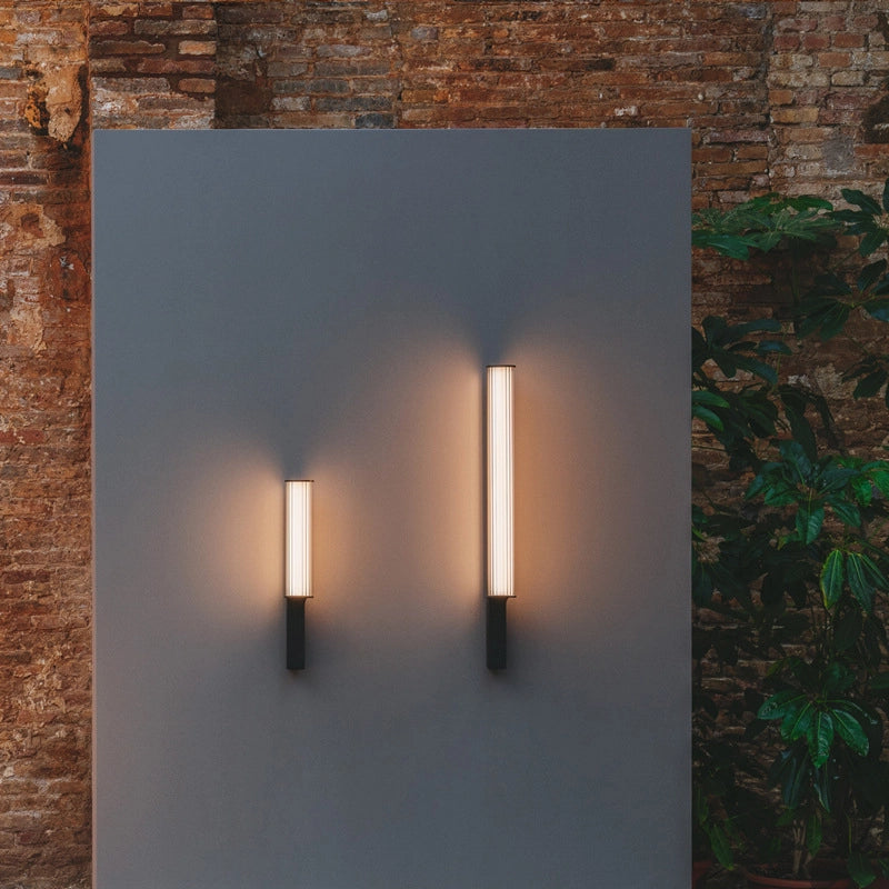 A pair of wall lamps, big and small, casting a warm glow on the exterior wall after dark